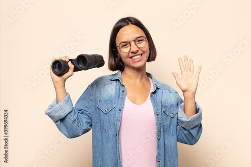 young latin woman smiling happily and cheerfully, waving hand, welcoming and greeting you, or saying goodbye photo