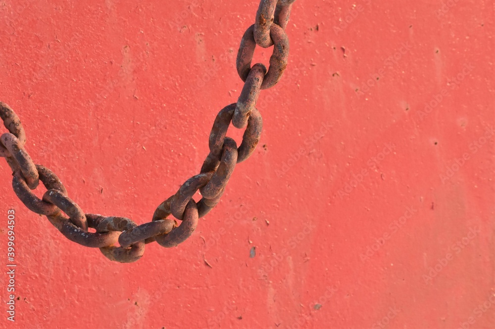 Rusty, weathered chain, with red painted background. Interesting curved line.