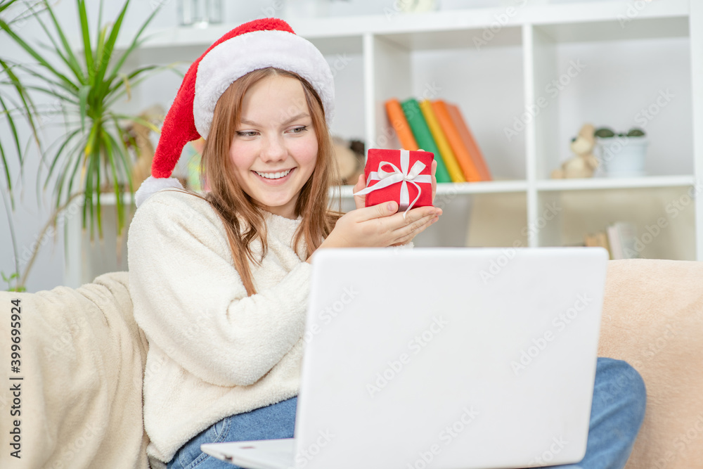 Happy Teen girl meets Christmas (New Year) through a video call with friends during pandemic coronavirus and shows gift box