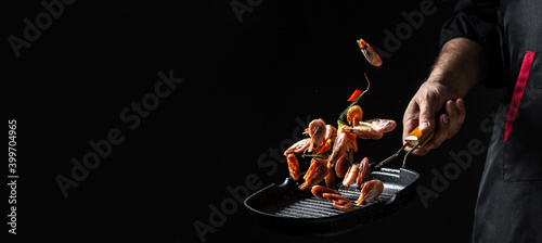 Obraz na plátně Chef hands cooking shrimps or prawn in pan on black background