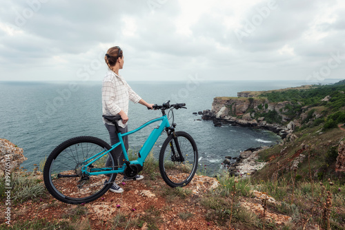 Woman with a bike in the nature / Morning view of a woman with an electric bike enjoys the view of the rocky Black Sea coast.