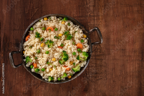 Vegan rice with vegetables, shot from above in a frying pan on a rustic wooden background with copyspace