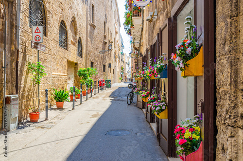 Narrow cobblestone street in Taranto historical city center. Typical italian street with flowers in pots, bicycle and stone walls of buildings in sunny day, Puglia Apulia, Italy © Aliaksandr