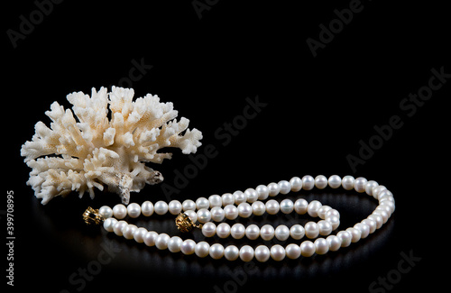 Natural pearl necklace, bracelet and branch of sea white coral isolated on black background. Copyspace for text