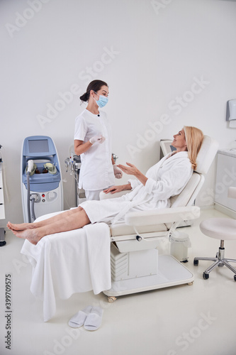 Good looking two women in white clothes talking together about spa treatment