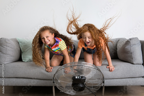 Two funny young girls on couch facing a fan