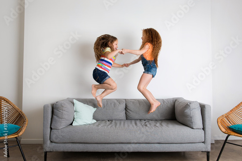 Two funny young girls jumping on sofa at home photo