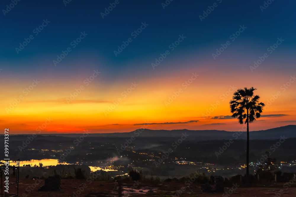 Silhouette palm tree on sunrise with colorful twilight sky on the mountain.