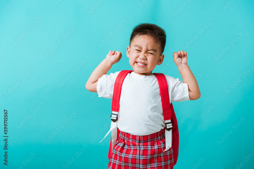 Back to school. Portrait happy Asian cute little child boy in uniform smile raise hands up glad when go back to school, isolated blue background. Kid from preschool kindergarten with school backpack Back to school. Portrait happy Asian cute little child boy in uniform smile raise hands up glad when go back to school, isolated blue background. Kid from preschool kindergarten with school backpack