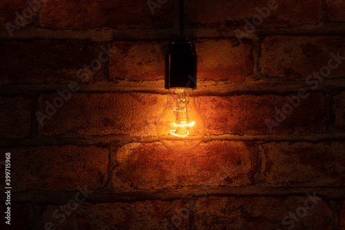 Single light bulb is on over a brick wall. photo