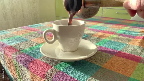 pouring small white espresso cup with fresh brewed hot coffee, daylight interior scene