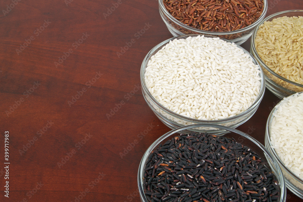 Different kinds of rice in bowls - white, brown, red and black rice.