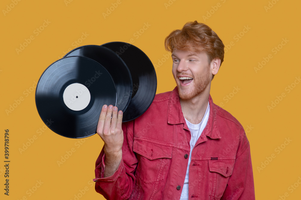 Red-haired bearded young man in red jacket with a record smiling Red-haired bearded young man in red jacket with a record smiling