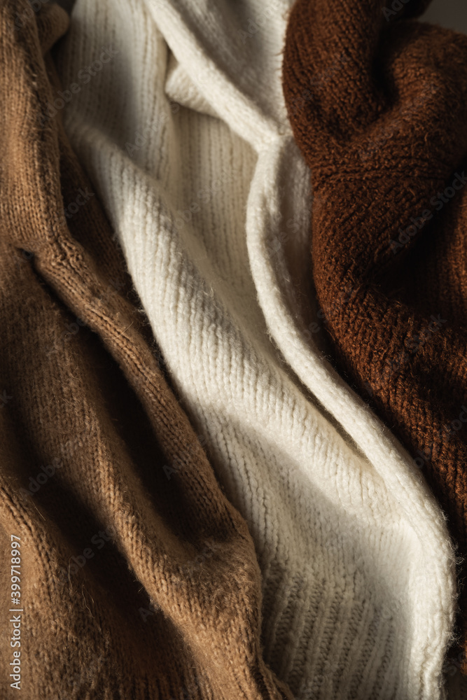 Fototapeta premium Three colorful warm woolen winter sweaters / pullovers. Beige, white, brown. Minimal fashion composition. Flat lay, top view.