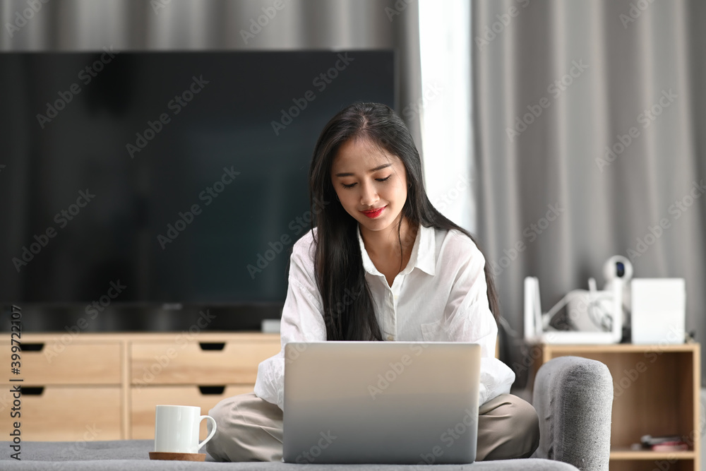Young female freelancer in casual wear sitting on couch and working on project with computer laptop. Young female freelancer in casual wear sitting on couch and working on project with computer laptop.
