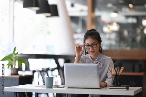 An attractive elegant businesswoman working with computer laptop and  touching the black rim of glasses.