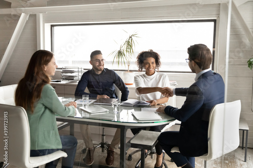 Happy multiethnic businesspeople handshake close deal or male agreement at team meeting in office. Smiling international business partners colleagues shake hands get acquainted greeting at briefing.