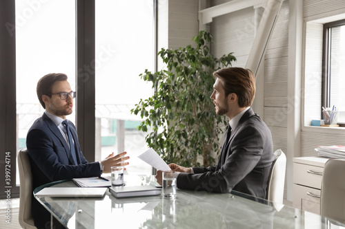 Concentrated Caucasian male businesspeople or partners talk discuss company paperwork document at meeting in office. Businessmen speak brainstorm, engaged in discussion at briefing in boardroom.