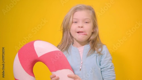 Little girl licks a huge striped lollipop. Close-up