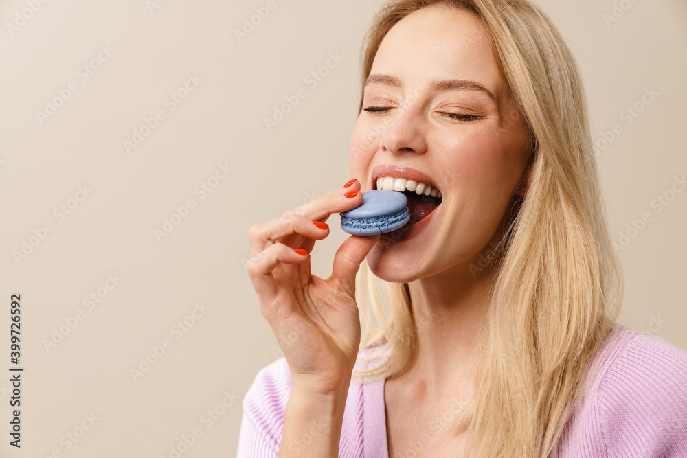 Cheerful beautiful girl eating macaroon with eyes closed
