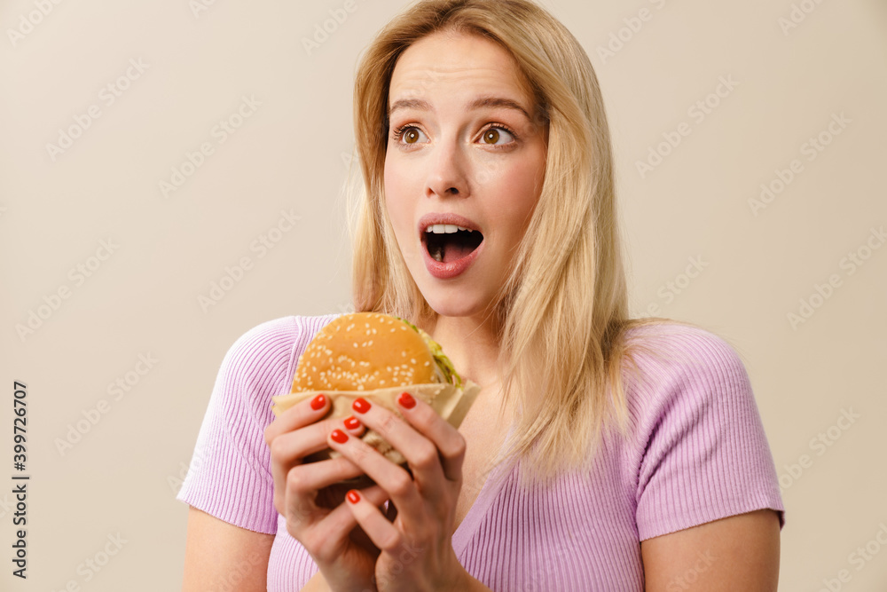 Surprised beautiful blonde girl posing with hamburger Surprised beautiful blonde girl posing with hamburger