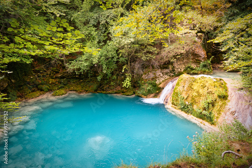 small river of turquoise water with a waterfall that ends in a pond © Adolf