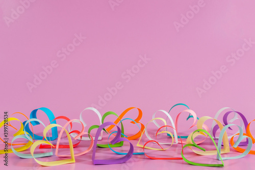 Multicolored paper Love hearts on pink background.