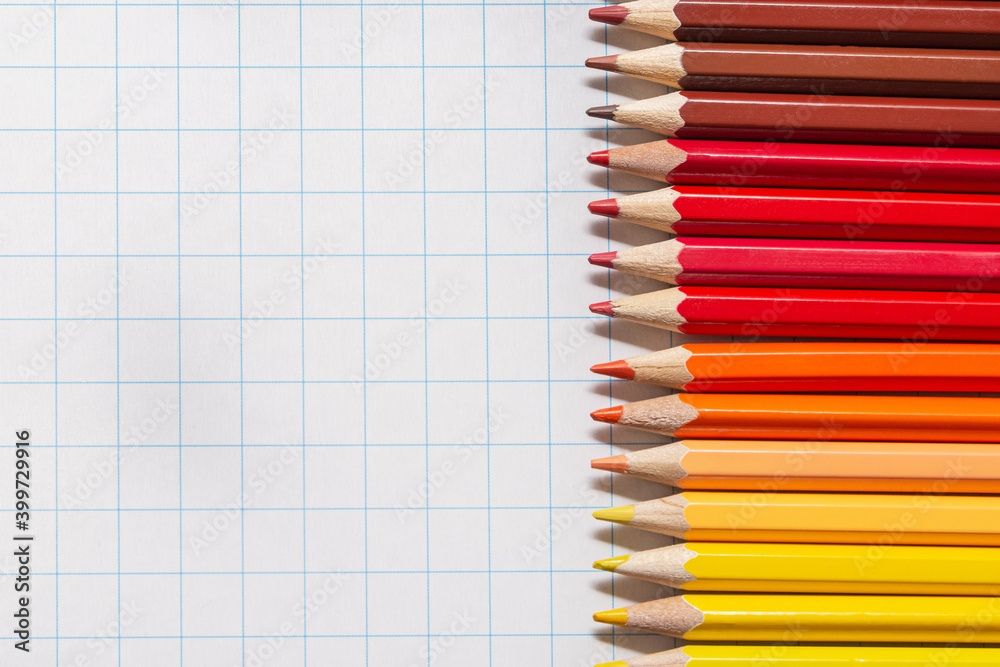 On a white checkered background there are wooden pencils of red, yellow, brown colors On a white checkered background there are wooden pencils of red, yellow, brown colors