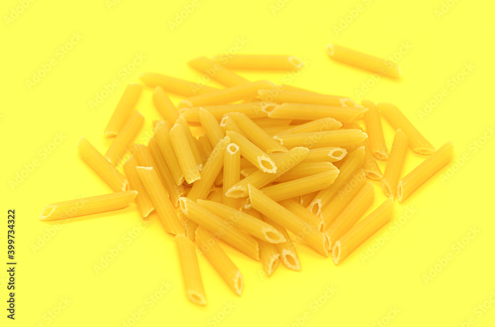 One serving of raw Penne pasta on yellow background. Classic extruded Variety of pasta from whole wheat varieties with cylinder-shaped pieces, their ends cut at a bias. One serving of raw Penne pasta on yellow background. Classic extruded Variety of pasta from whole wheat varieties with cylinder-shaped pieces, their ends cut at a bias.