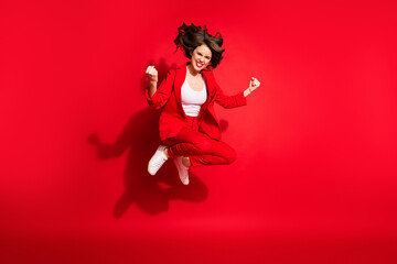 Full length photo of funky lovely young girl crazy jump fists wear jacket trousers footwear isolated red color background