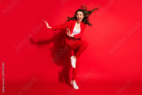 Full length photo of lovely young girl wind blow hairdo raise knee look side empty space wear jacket pants footwear isolated red color background