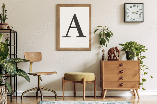 Vintage interior design of living room with design retro furnitures, plants, shelf, black clock and brown poster mock up frame on the beige wall. Stylish home decor. Template.