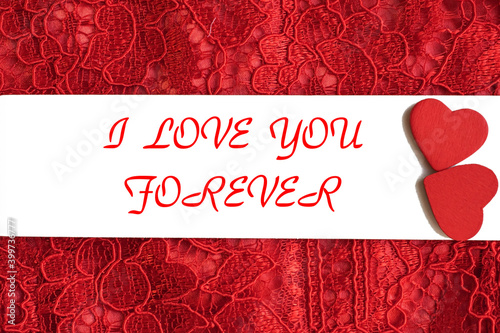 I love you forever is written on a white horizontal sheet with two hearts lying on a red openwork background.