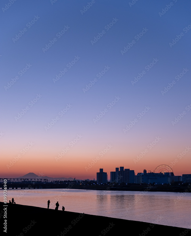 Sunset at Kyuedo River with silhouette of Mount Fuji and Maihama Great Bridge in the background and a person fishing by the river in the foreground. Sunset at Kyuedo River with silhouette of Mount Fuji and Maihama Great Bridge in the background and a person fishing by the river in the foreground.