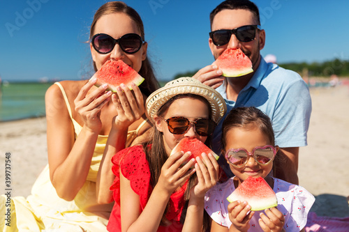 family, leisure and people concept - happy mother, father and two daughters having picnic on summer beach and eating watermelon and having fun © Syda Productions