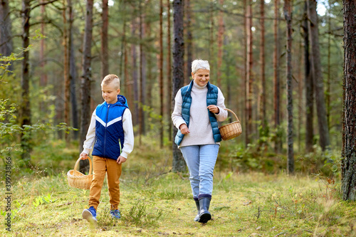 picking season  leisure and people concept - happy smiling grandmother and grandson with baskets and mushrooms in forest