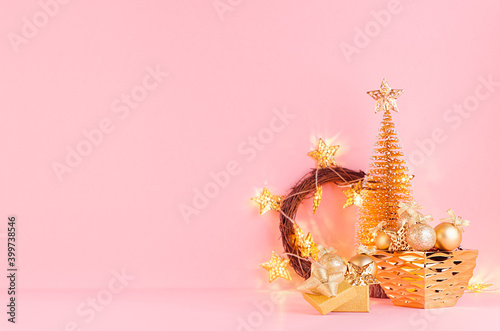 Christmas background in gold glitter color - christmas tree, wreath, balls, bowl and glowing star lights on light pink background, copy space.