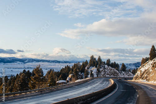 Highway in beautiful place in winer on the summer day. Landscape with asphalt road, trees, snow-covered mountain in winter. Montana, USA, 12-2-2019