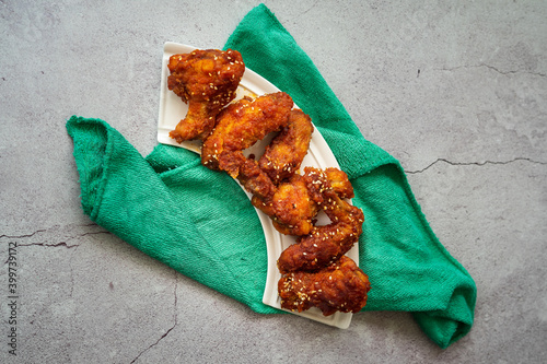 Deep fried chicken wings and drummets coated with hot and spicy Korean sauce on a white plate and green cloth. photo