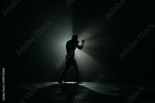 Fighter striking a blow. Professional sport. Fighting. Strength. Fighter in a moody light and grain mood. 
boxer training with punching bag in dark sports hall