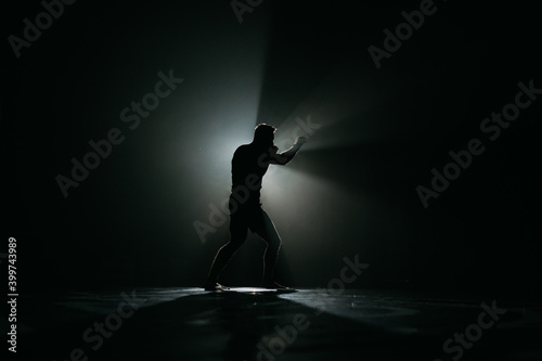 Fighter striking a blow. Professional sport. Fighting. Strength. Fighter in a moody light and grain mood. boxer training with punching bag in dark sports hall