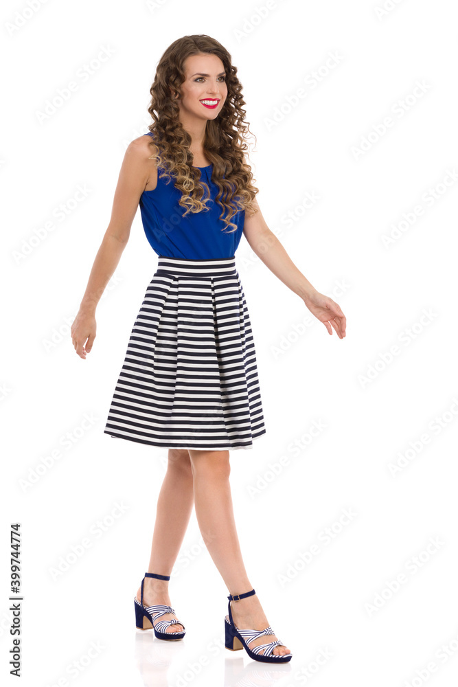 Young Woman Is Walking In Striped Skirt And High Heels And Looking Away. Side View. Young Woman Is Walking In Striped Skirt And High Heels And Looking Away. Side View.