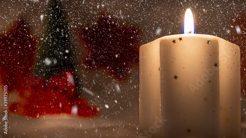 Burning white candle in snowing background witj red snowflake