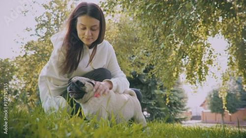 A young woman is sitting in the park with her pug.