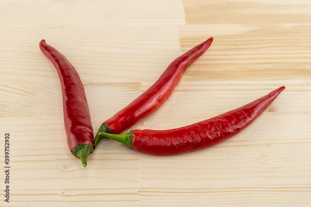 Long pods of hot red chili peppers spread out on a fan on a wooden background
