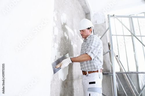 plasterer man at work with trowel plastering the wall of interior construction site wear helmet and protective gloves, scaffolding on background and copy space on white wall