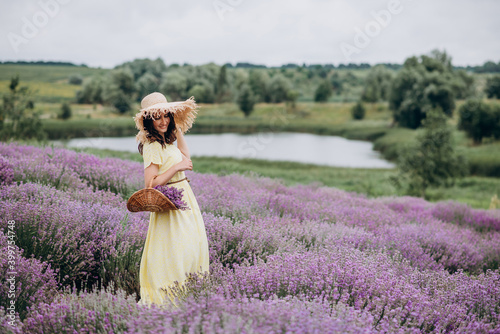 Beautiful carefree woman in dress and hat with a basket of flowers in a field of fragrant lavender. Soft selective focus, art noise