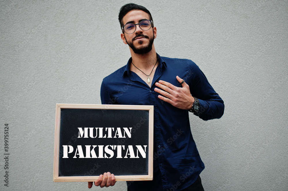 Arab man wear blue shirt and eyeglasses hold board with Multan Pakistan inscription. Largest cities in islamic world concept.