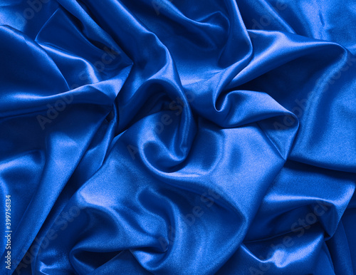 Elegant smooth royal blue satin, silk fabric drapes. Luxurious cloth textile with liquid wave. Abstract background or template. Fabric shiny glitter texture. Luxurious blue background.