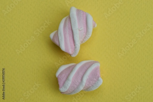 two colored pink white candy marshmallows lie on a yellow table